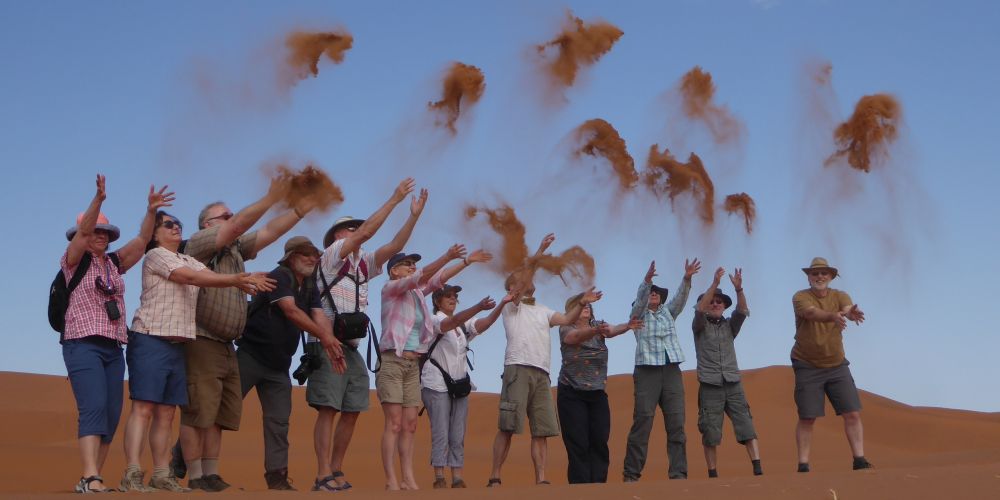 TARUK-Reisegruppe wirft auf einer Düne bei Sossusvlei roten Sand in die Luft